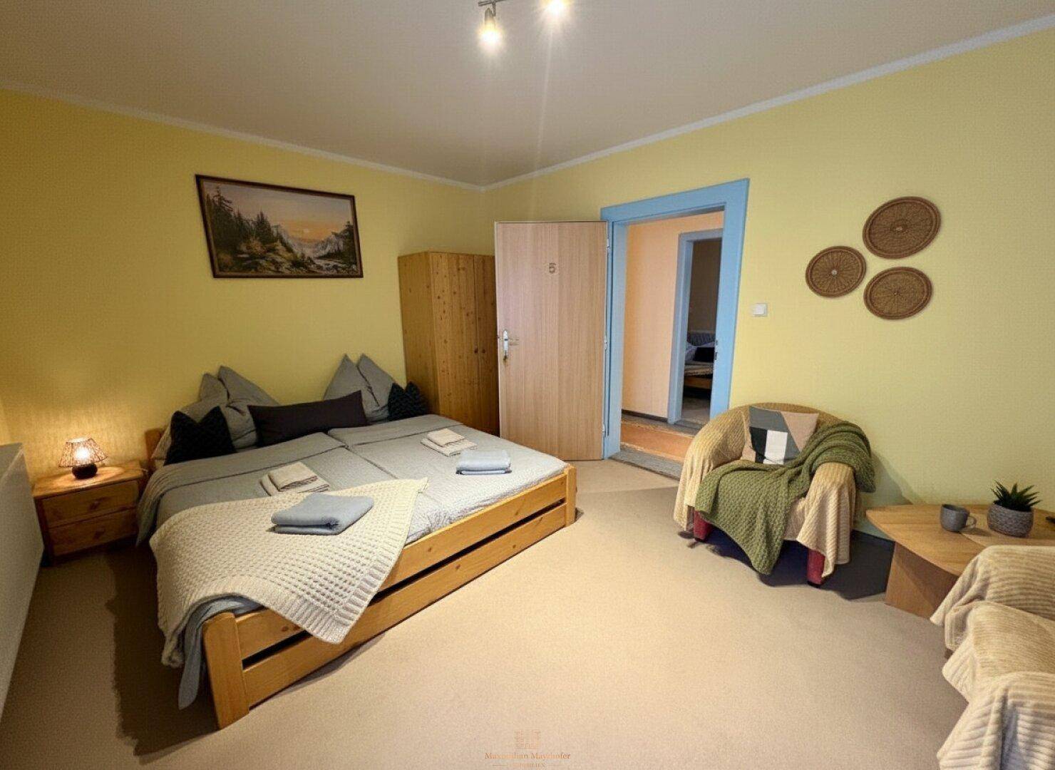 Schlafzimmer mit Doppelbett, Sessel und gelben Wänden, die eine warme Atmosphäre schaffen.