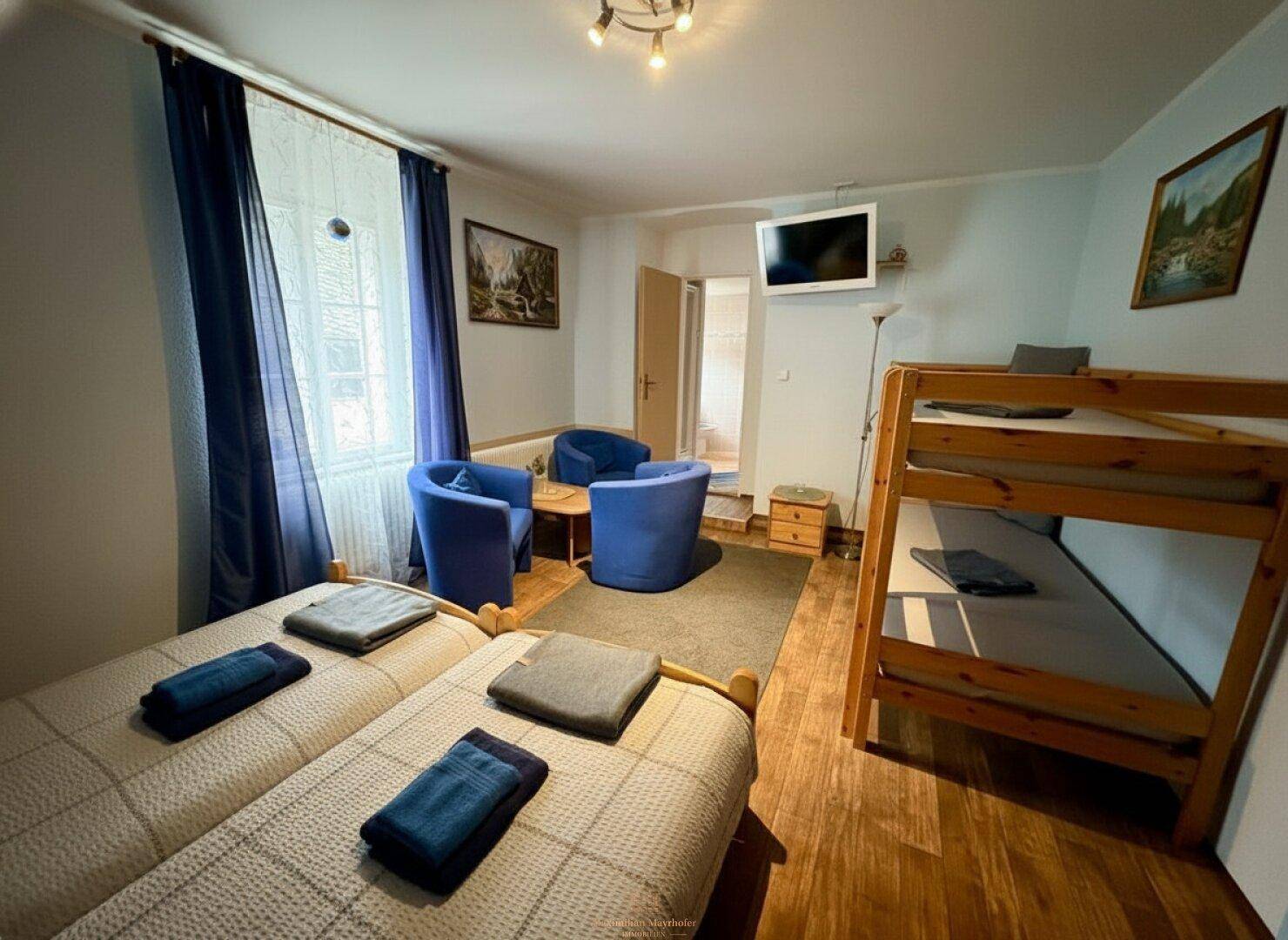 Geräumiges Schlafzimmer mit zwei Einzelbetten, einem Etagenbett und blauen Sesseln.