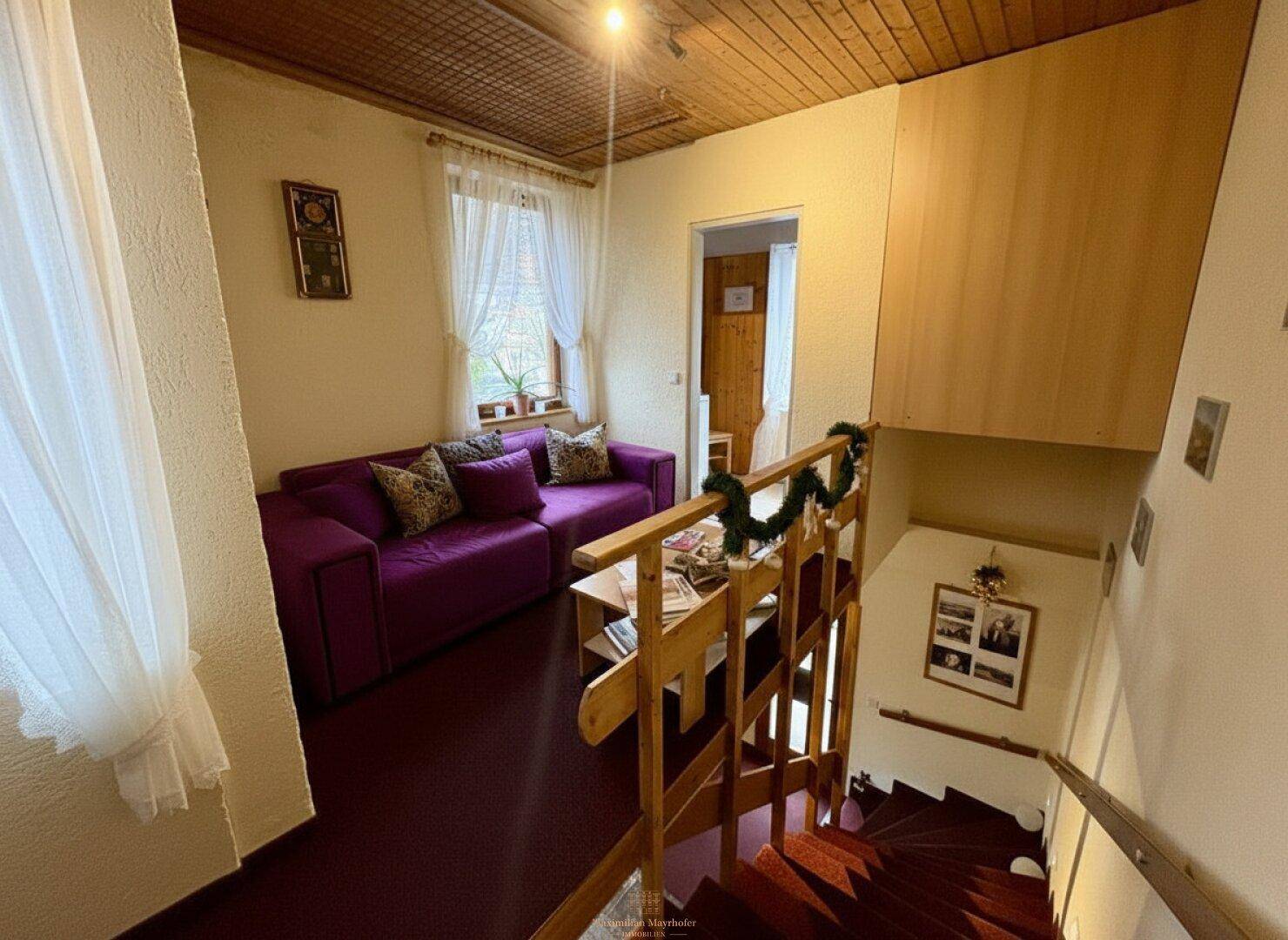 Wohnbereich mit violetter Couch, Holzdecke und Treppe, die zu weiteren Räumen führt.