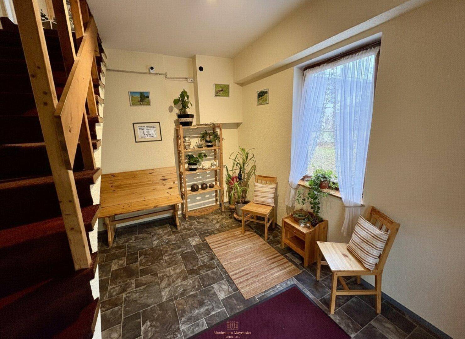 Gemütlicher Eingangsbereich mit Holztreppe, Fliesenboden und einem Fenster mit Vorhängen.