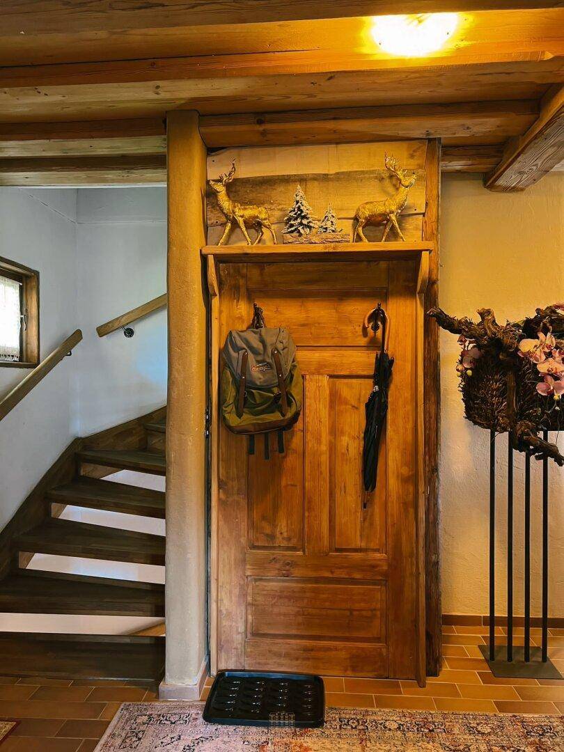 Rustikaler Eingangsbereich mit Holztreppe, Holztür und alpinen Dekorationselementen.