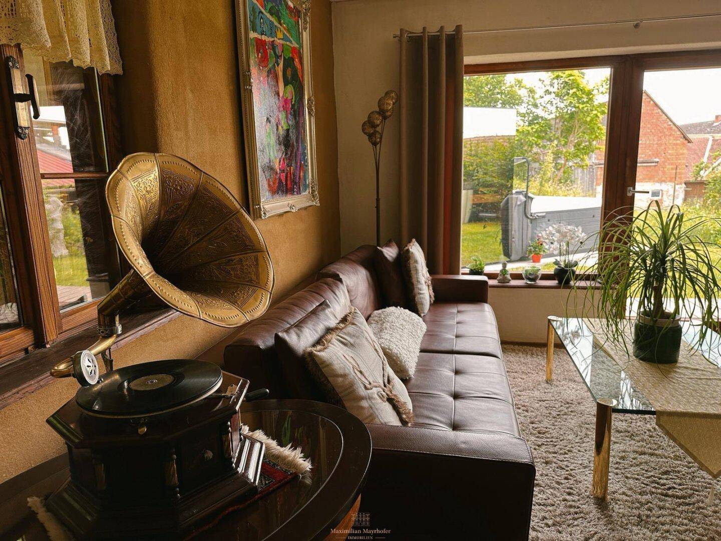 Wohnzimmer mit braunem Ledersofa, antikem Grammophon und Blick in den Garten.