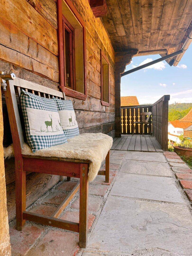 Überdachter Balkon mit Holzbank und Blick auf die umliegende Dorflandschaft.