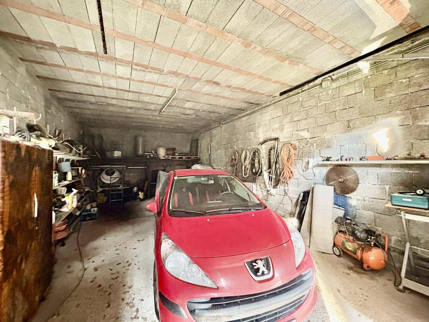 Geräumige Garage mit einem roten Auto und verschiedenen Werkzeugen und Lagerregalen.