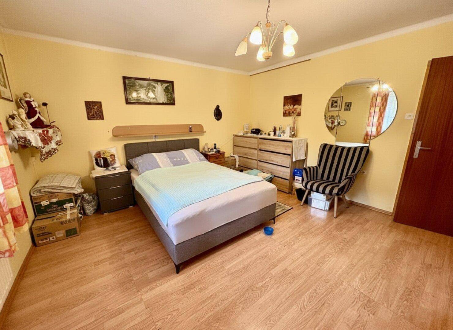Helles Schlafzimmer mit Doppelbett, Laminatboden und gelben Wänden, bietet eine freundliche Atmosphäre.