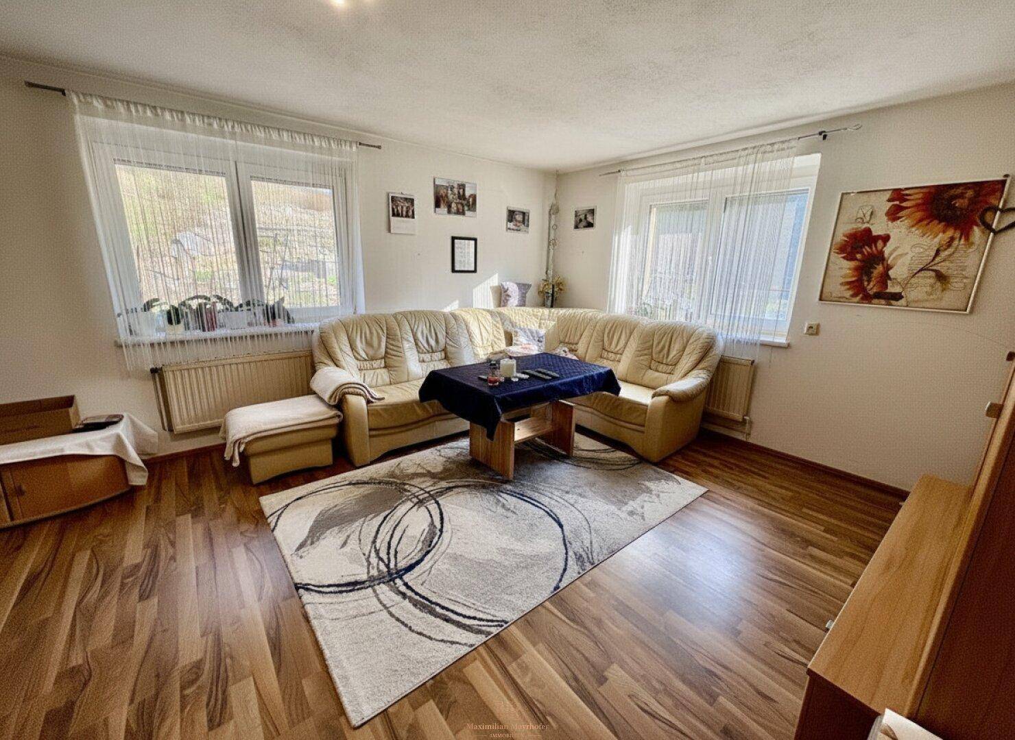 Helles Wohnzimmer mit beiger Ledercouch, Holzboden und zwei Fenstern für viel Tageslicht.