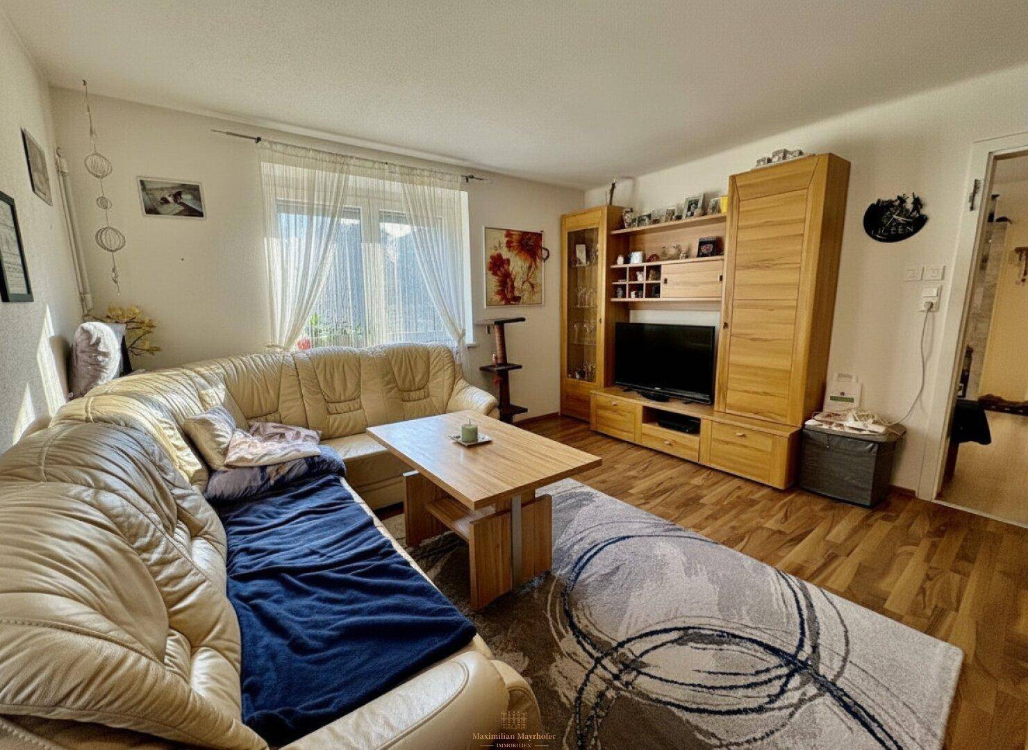 Gemütliches Wohnzimmer mit beiger Ledercouch, Holzmöbeln und einem Teppich als Akzent.