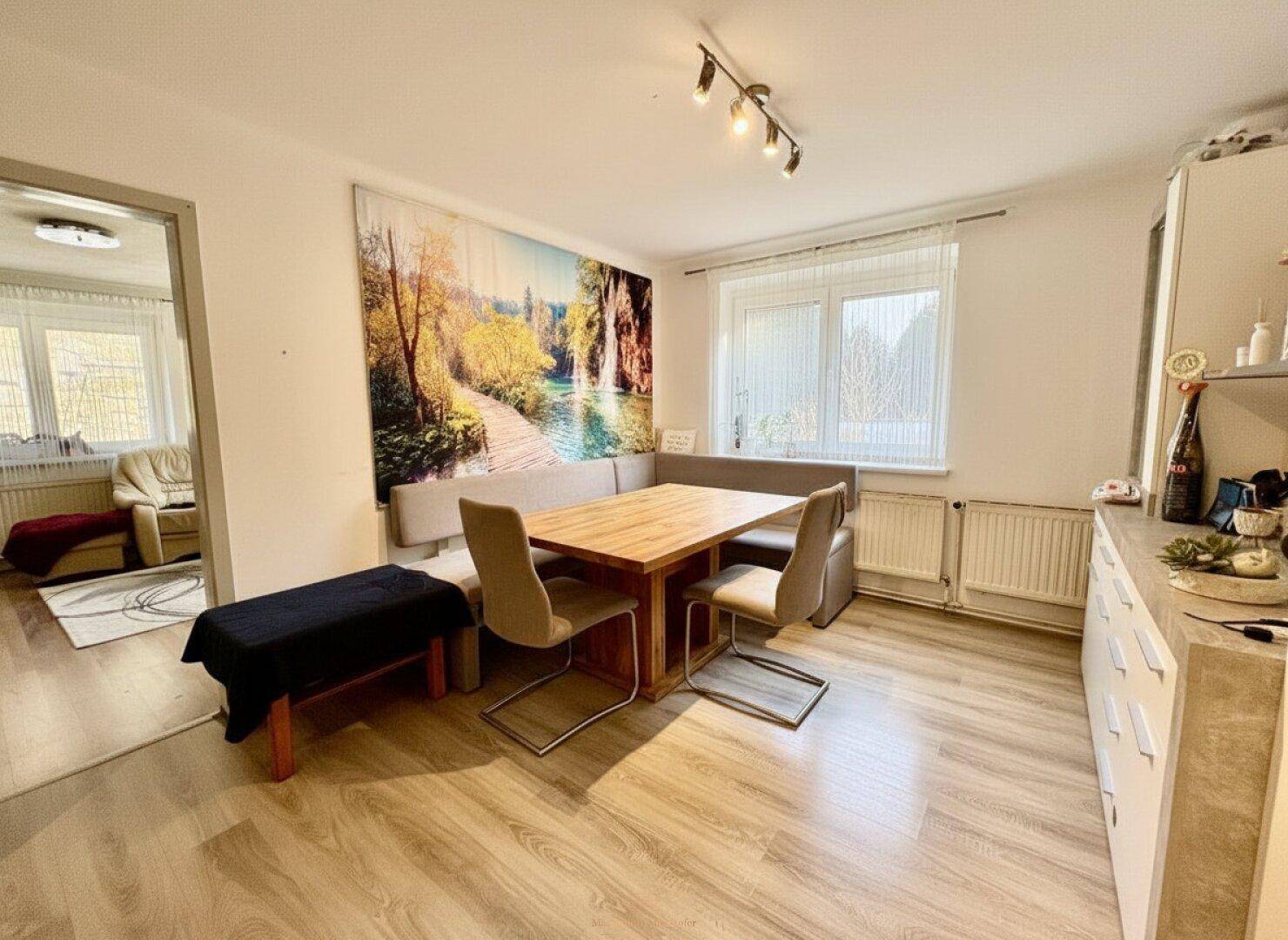 Gemütlicher Essbereich mit Holztisch, Eckbank und Blick ins Grüne durch das Fenster.