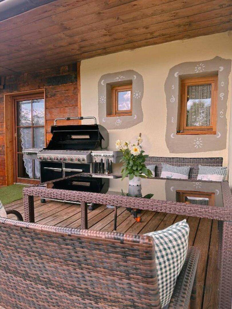 Gemütlicher Essbereich im Freien mit Grill und Rattanmöbeln auf einer Holzterrasse.