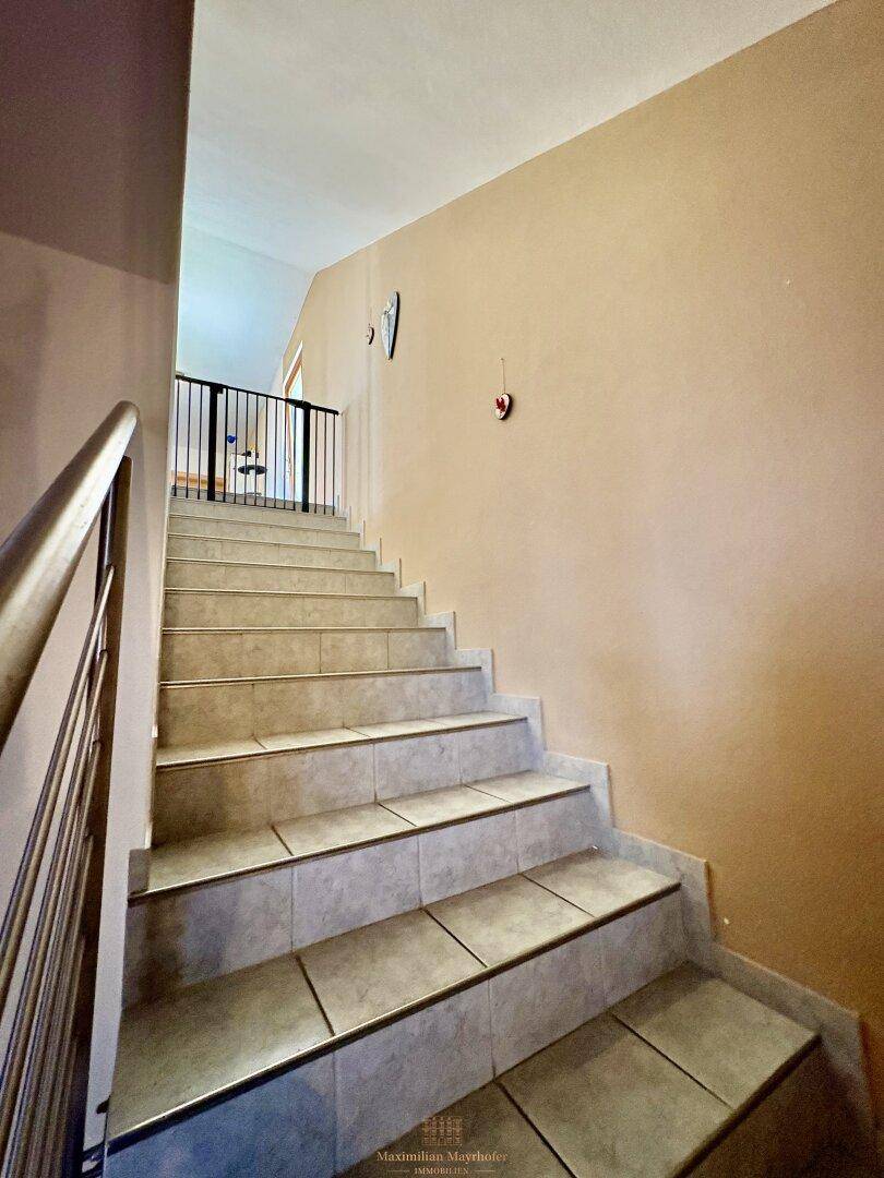 Treppenhaus mit Fliesenstufen und beigefarbenen Wänden, das in die obere Etage führt.