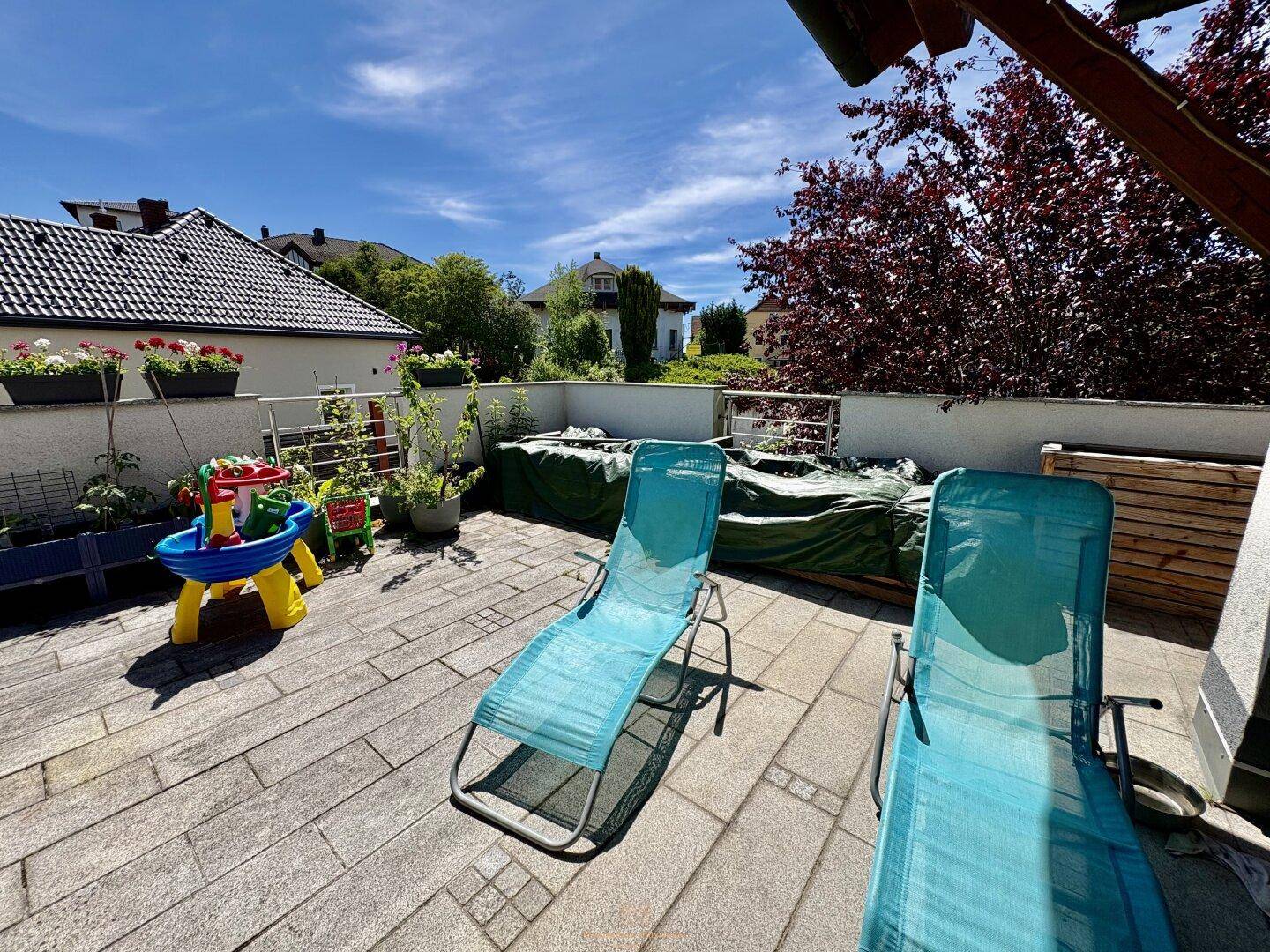 Sonniger Terrassenbereich mit Liegestühlen und Kinderspielzeug, ideal für Entspannung im Freien.