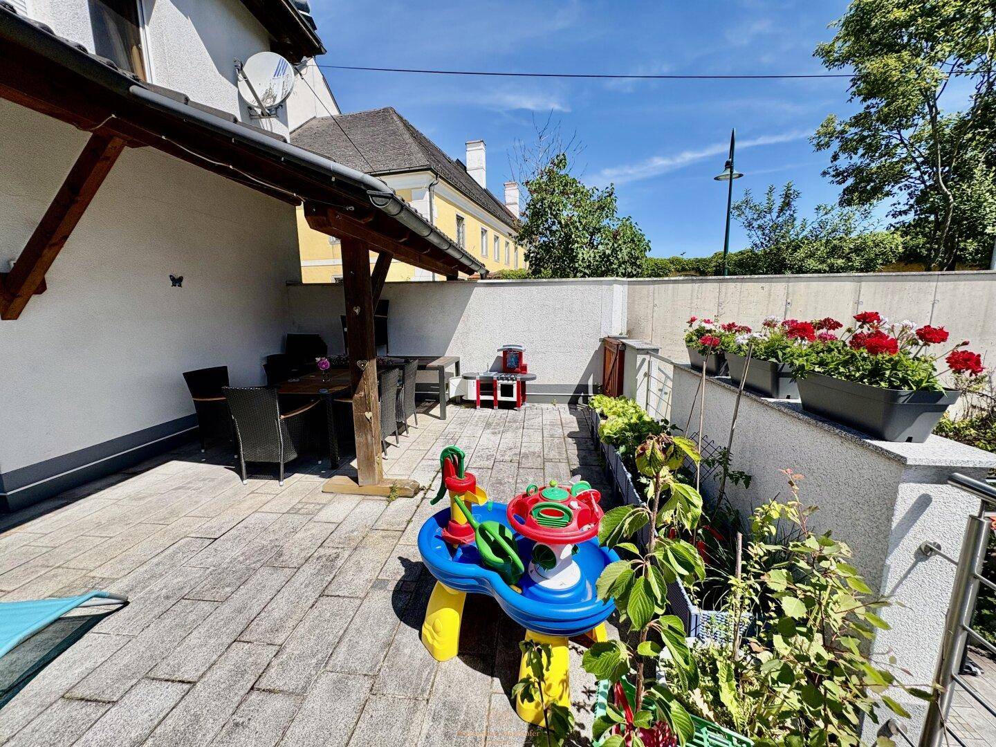 Große gepflasterte Terrasse mit Essbereich im Freien und Spielmöglichkeiten für Kinder.