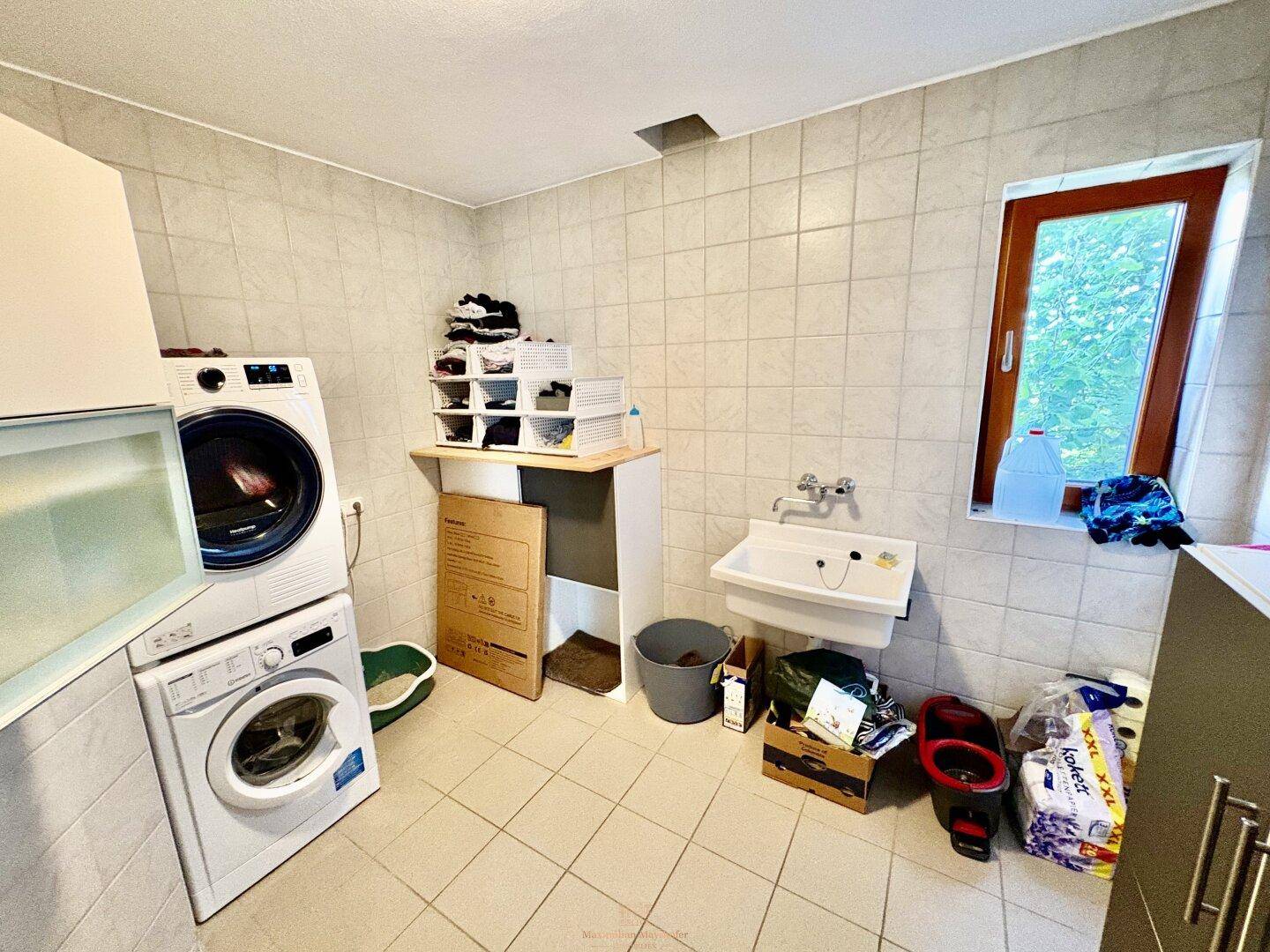 Praktischer Hauswirtschaftsraum mit Waschmaschine, Trockner und Waschbecken, komplett gefliest.