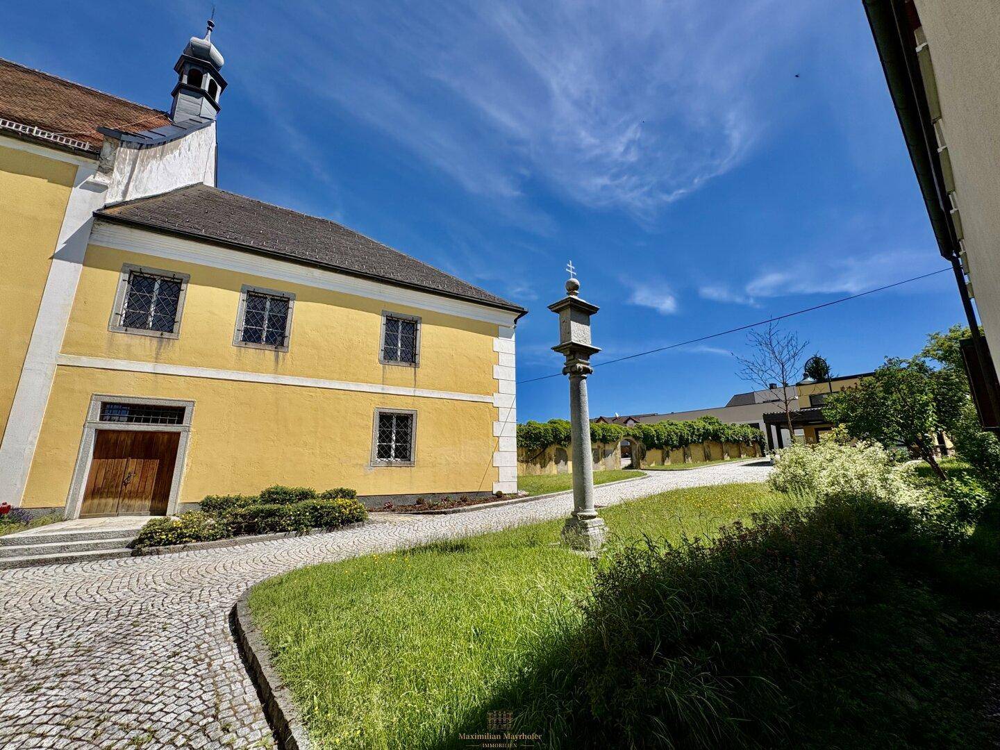 Seitenansicht des historischen Kirchengebäudes mit Kopfsteinpflasterweg und grüner Umgebung.