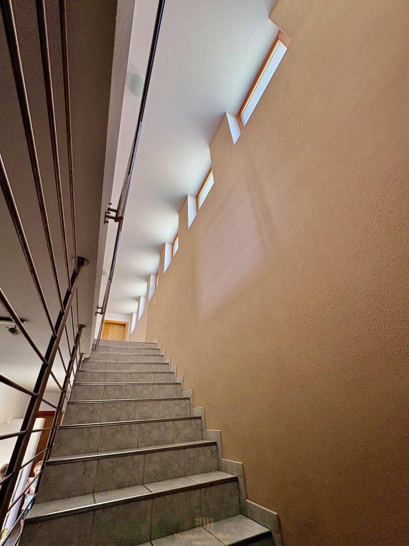 Heller Treppenaufgang mit Fliesenstufen und kleinen Fenstern, die natürliches Licht hereinlassen.