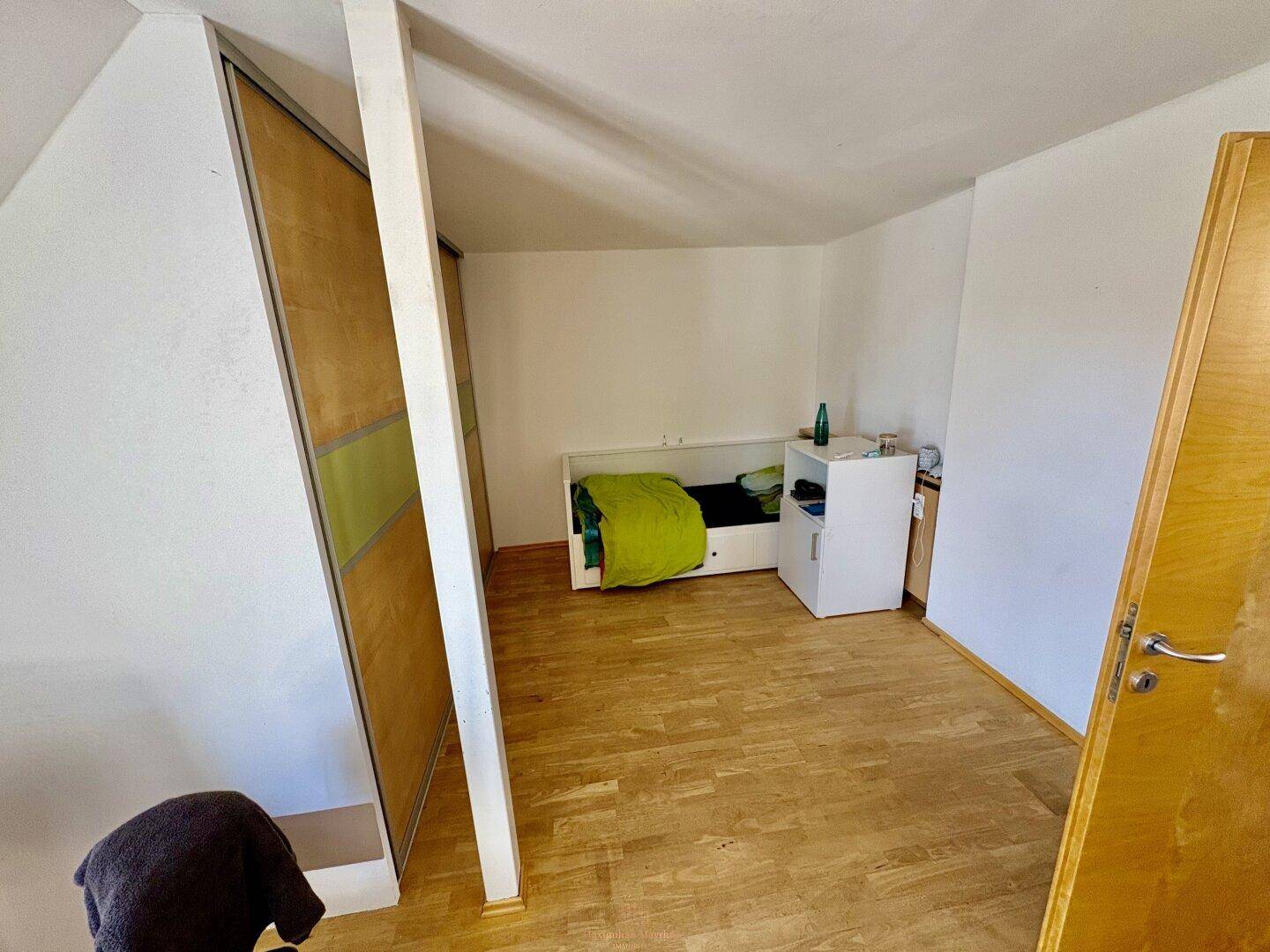 Helles Schlafzimmer mit Holzboden, integriertem Kleiderschrank und einfacher Einrichtung.