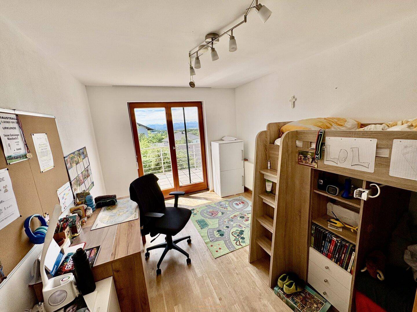 Kinderzimmer mit Hochbett, Schreibtisch und Zugang zu einem Balkon mit schöner Aussicht.