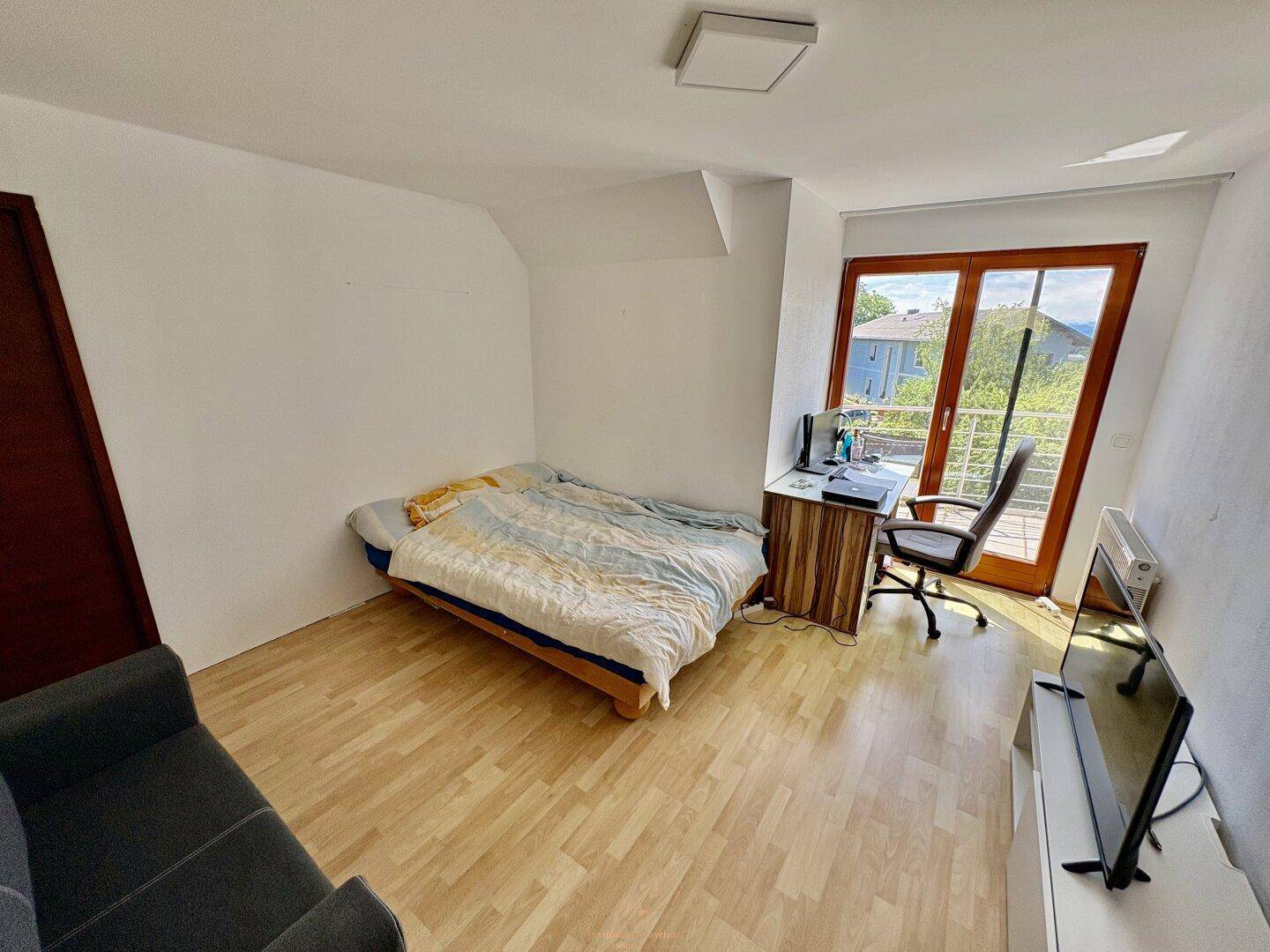 Schlafzimmer mit Bett, Schreibtisch und Balkonzugang, bietet einen hellen und funktionalen Raum.