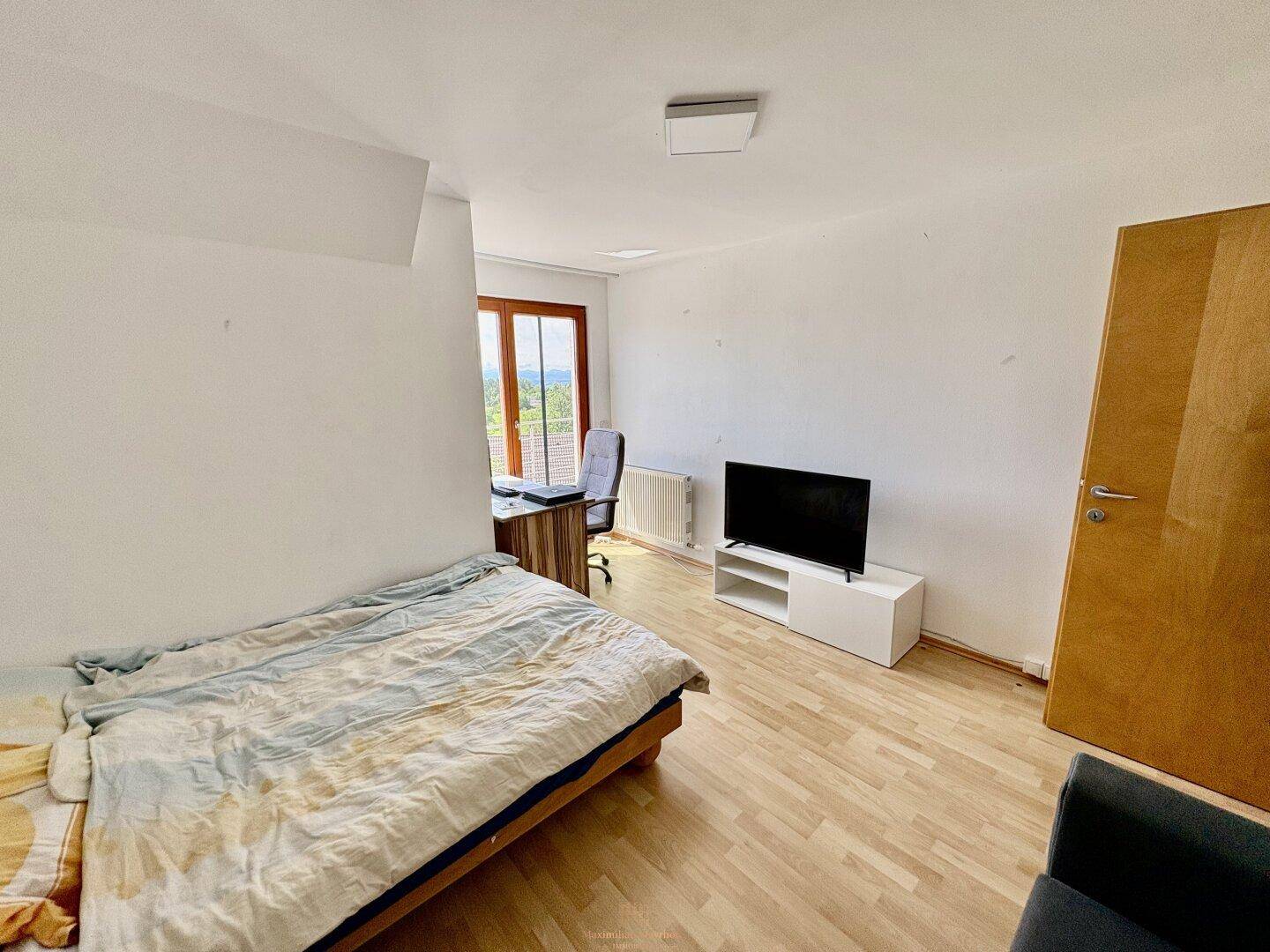 Helles Schlafzimmer mit Holzboden, Bett, Schreibtisch und Fernseher, ideal für Ruhe und Arbeit.