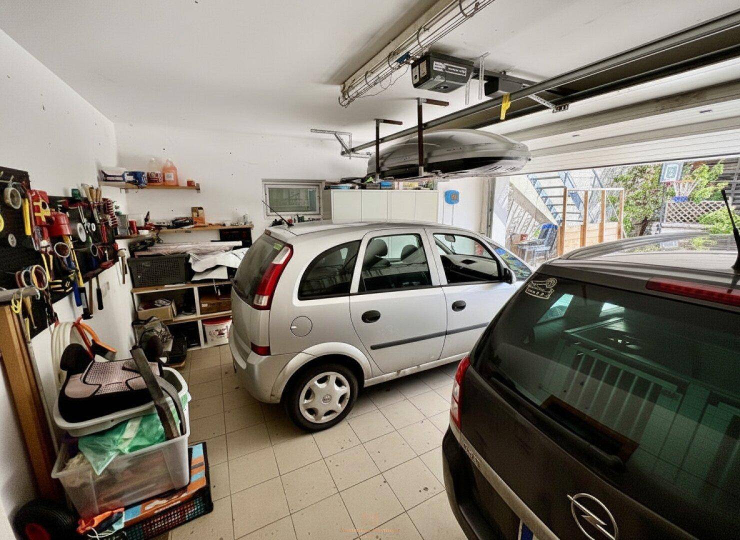 Geräumige Garage mit zwei geparkten Autos und Regalen für Werkzeuge und Lagerung.