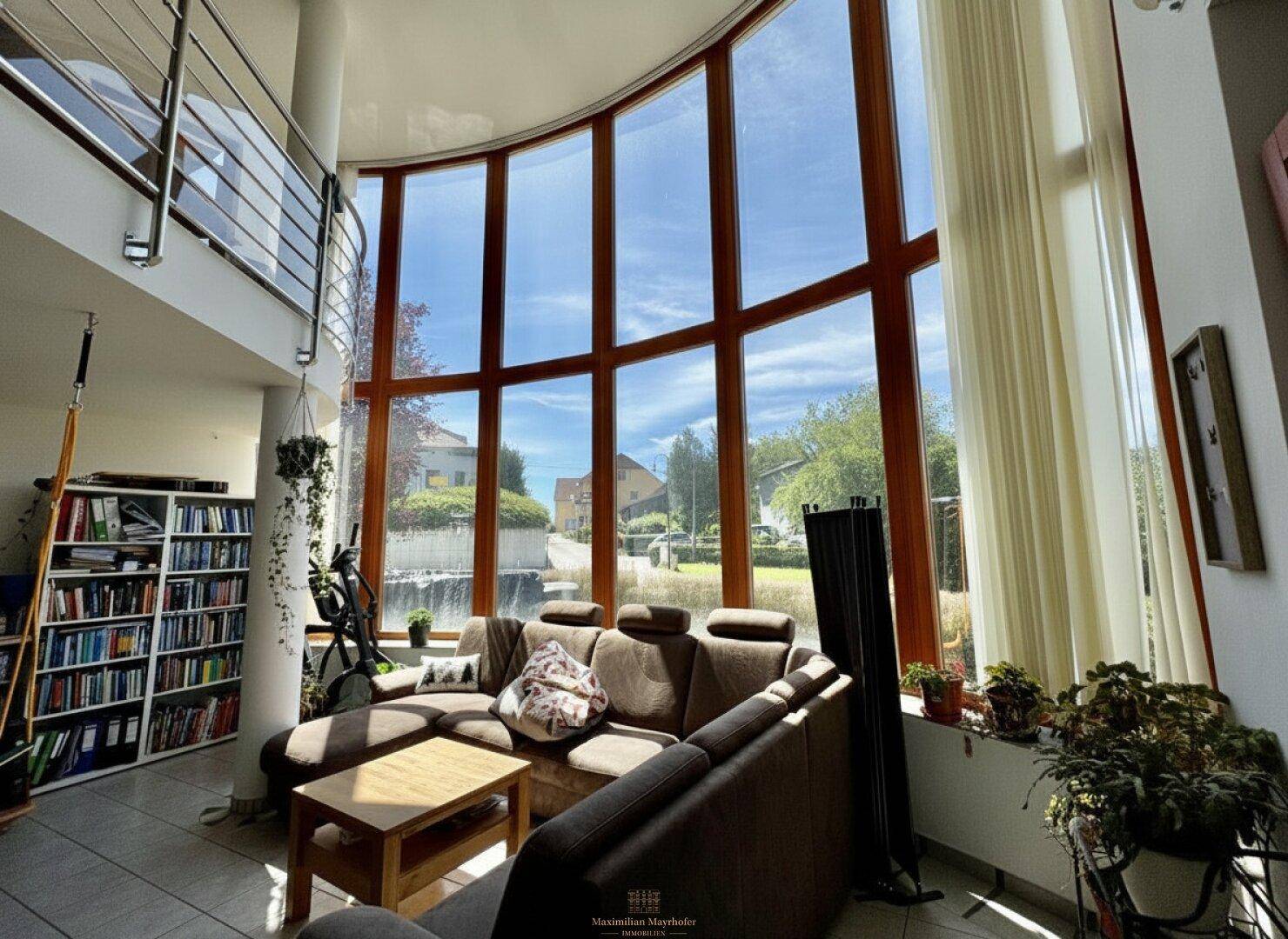 Lichtdurchflutetes Wohnzimmer mit hohen Fenstern, bequemer Couch und Bücherregal.