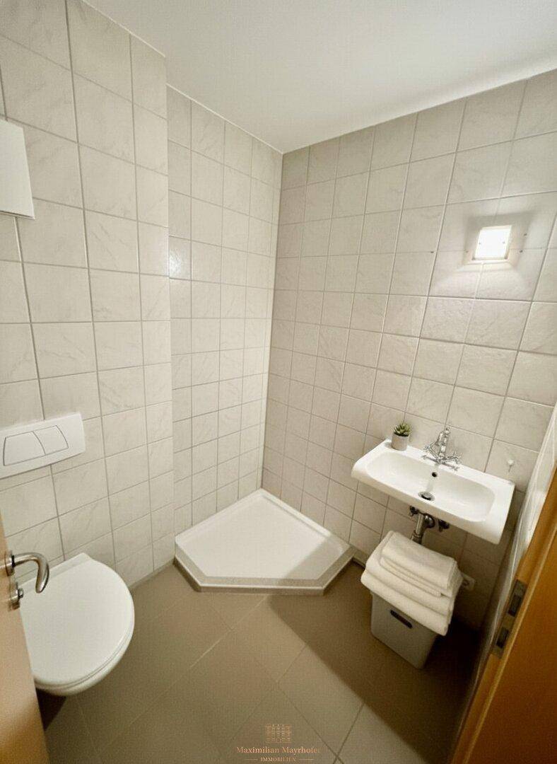 Kleines Badezimmer mit hellen Fliesen, Dusche, WC und Waschbecken.