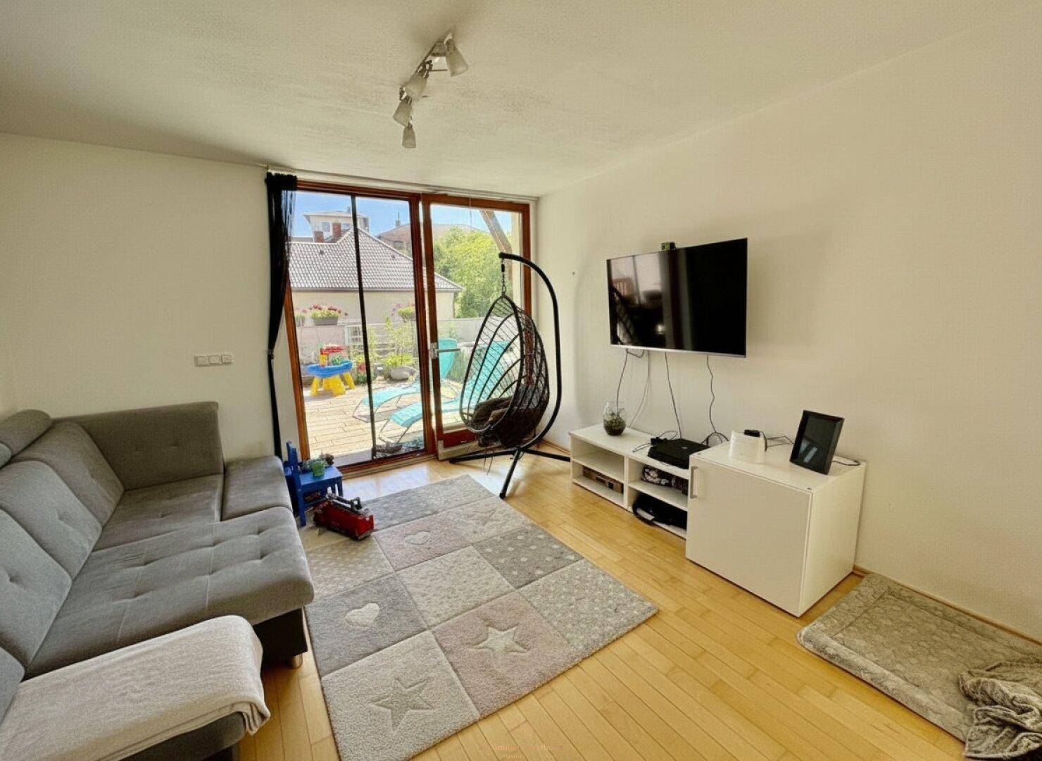 Helles Wohnzimmer mit Zugang zur Terrasse, ausgestattet mit einem bequemen Sofa und Fernseher.