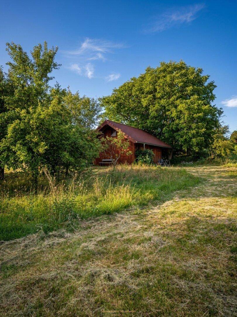 Charmantes Holzhaus mit rotem Dach, umgeben von üppigem Grün und Wiesenfläche unter blauem Himmel.