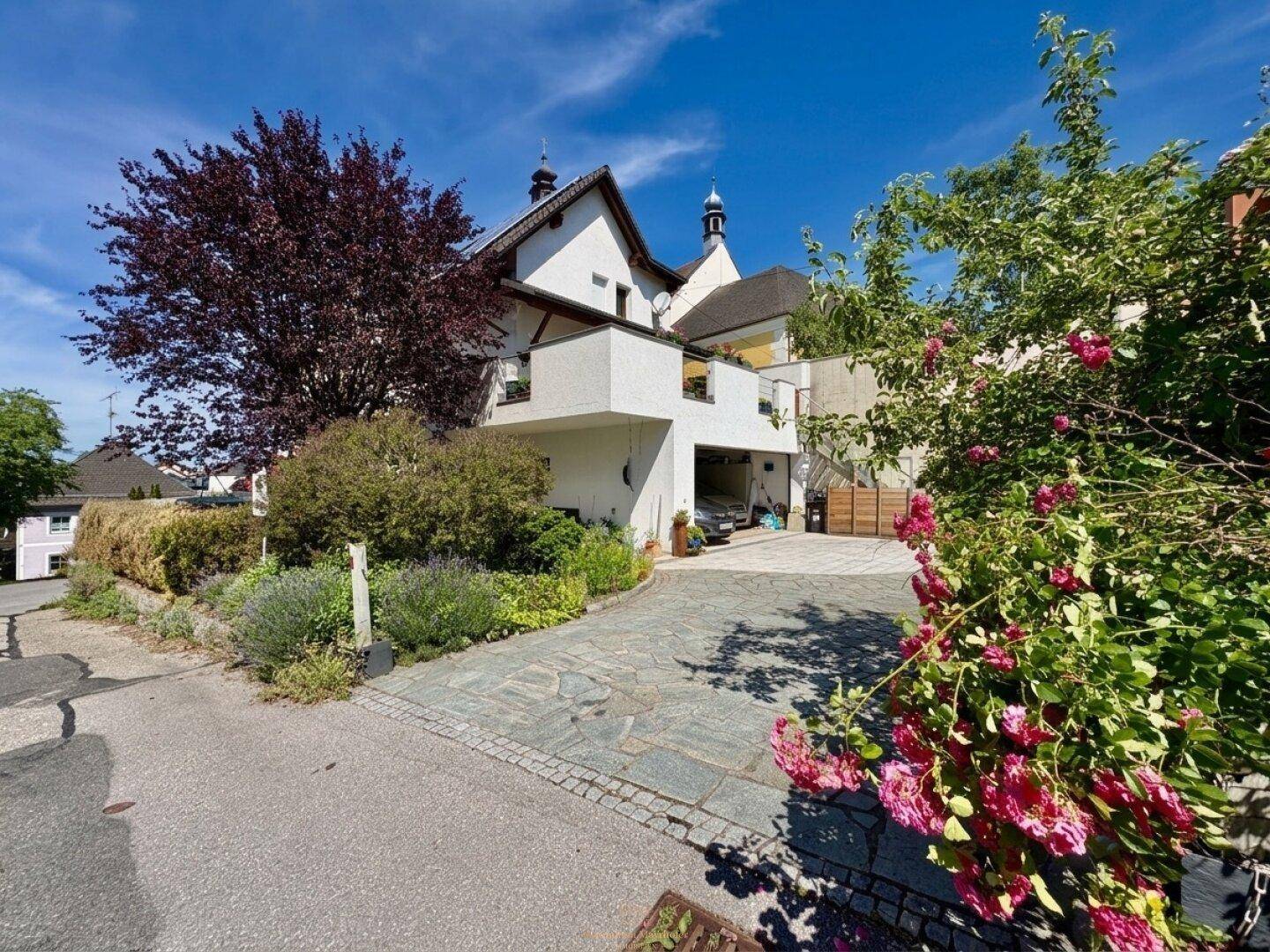 Haus mit gepflasterter Auffahrt und blühenden Rosenbüschen im Vorgarten.