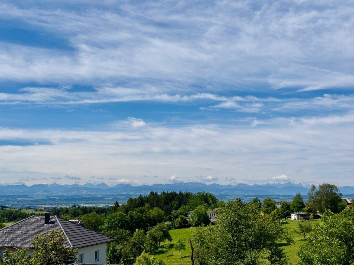 Weitläufiger Panoramablick auf die Alpen und die umliegende grüne Landschaft unter blauem Himmel.