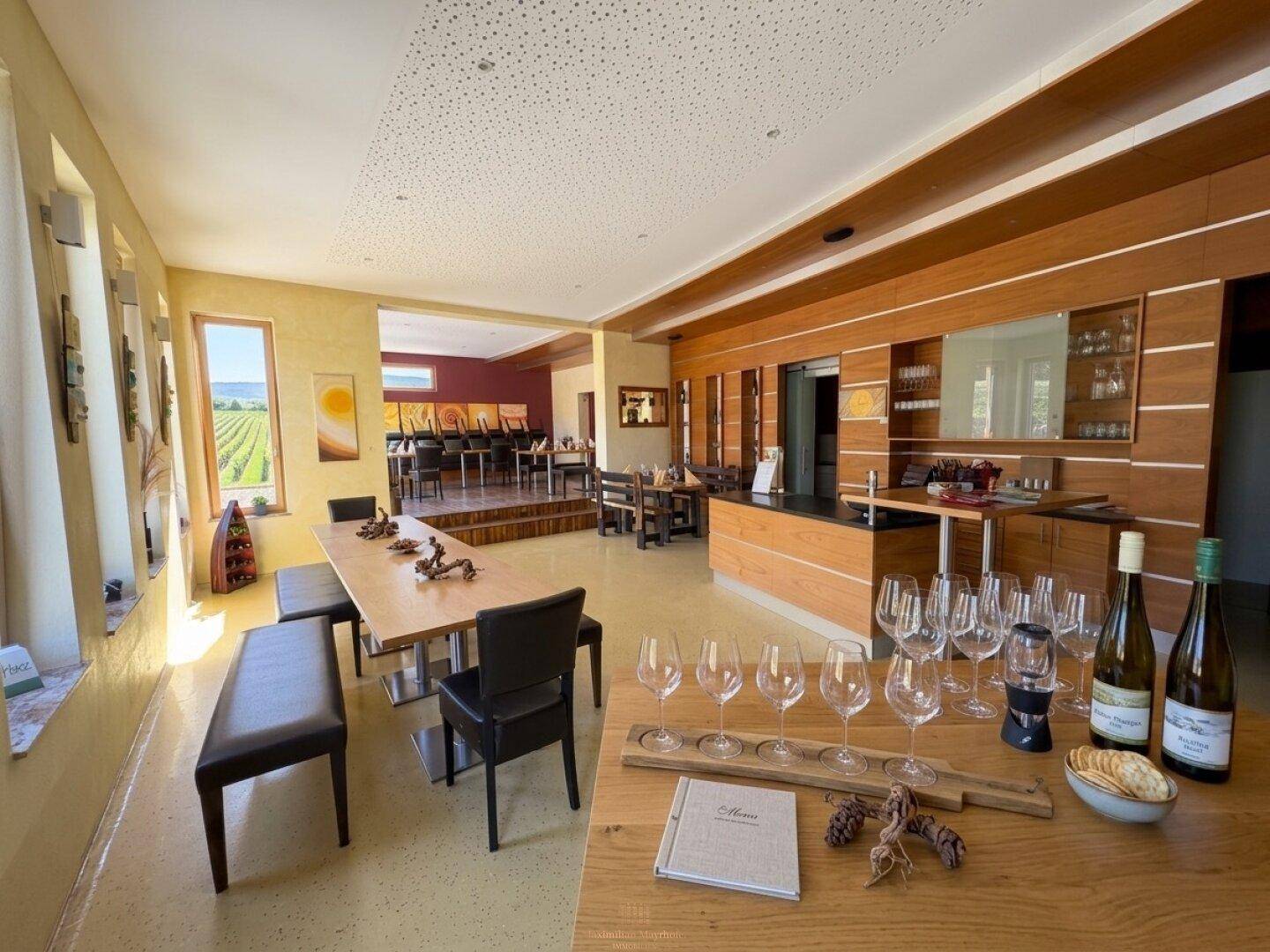 Geräumiger Verkostungsraum mit Holzelementen, langen Tischen und Blick auf die Weinberge.