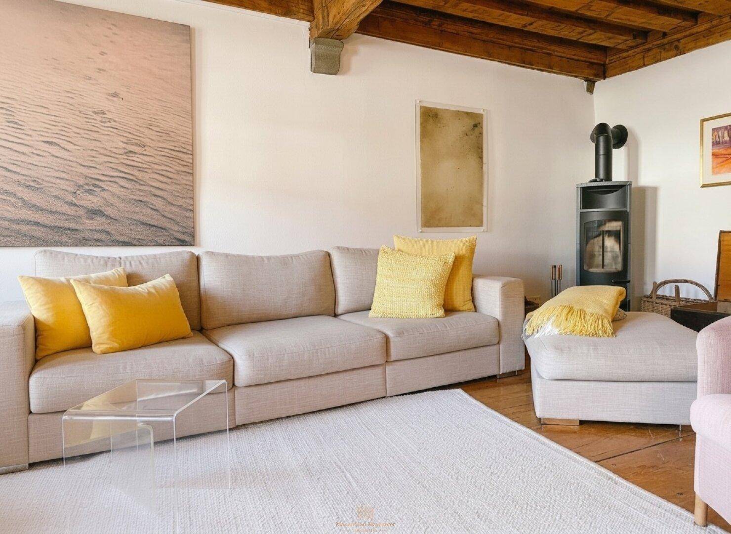 Helles Wohnzimmer mit Holzbalkendecke, modernem Sofa und einem Kaminofen.