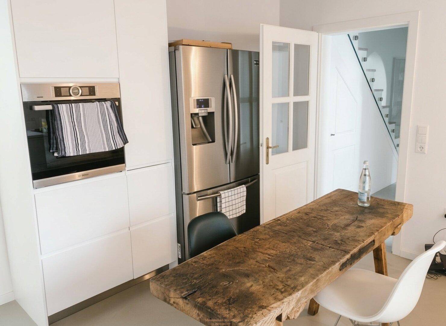 Funktionale Küche mit integriertem Backofen, großem Kühlschrank und rustikalem Holztisch.