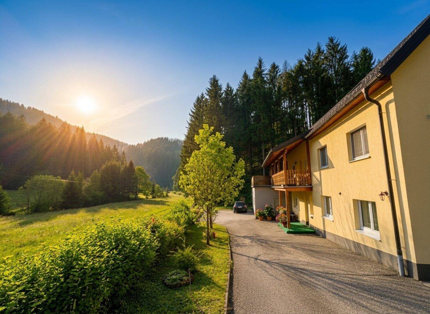 Sonnenuntergang über dem gelben Haus, umgeben von grünen Wiesen und dichten Wäldern.