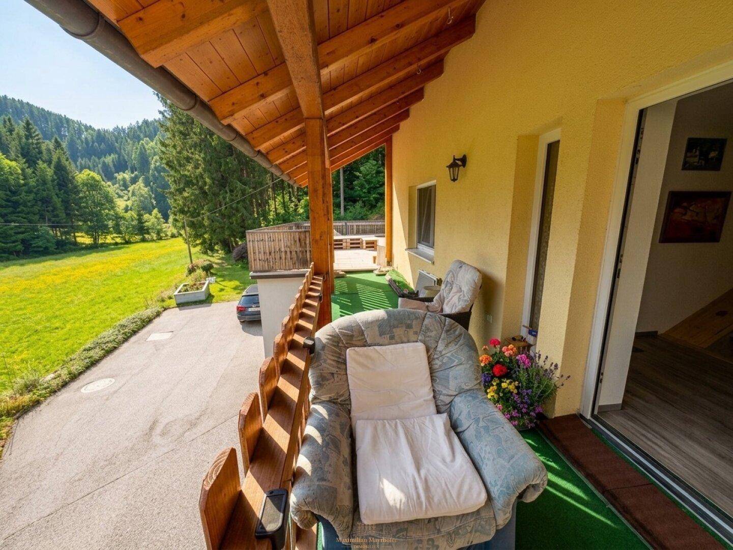 Überdachter Holzbalkon mit Sitzgelegenheiten und weitem Blick auf die umliegende Natur.