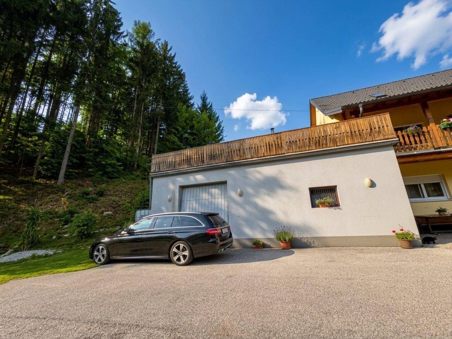 Gelbes Haus mit Garage und geparktem Auto, umgeben von Wald und Natur.