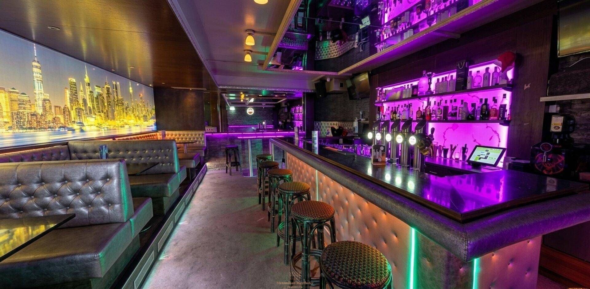 Lange Bar mit beleuchteten Regalen, bequemen Sitzbänken und einer Wandmalerei der New Yorker Skyline.