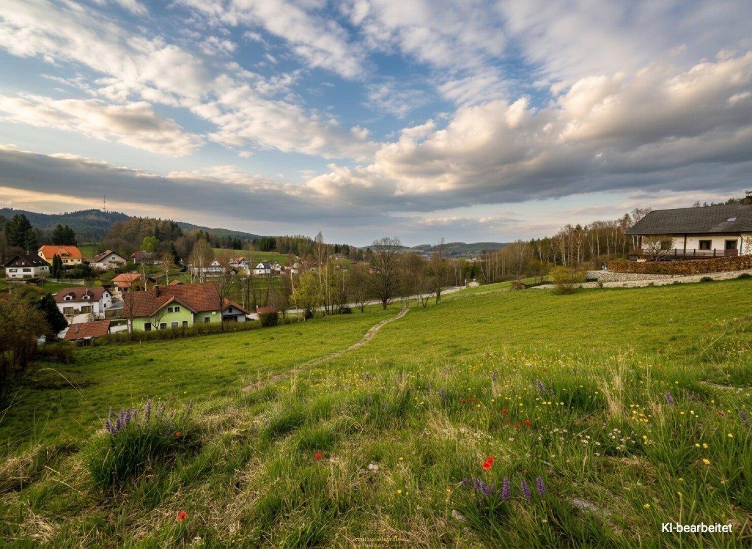 Weitläufige Landschaft mit einem malerischen Dorf, umgeben von grünen Wiesen und sanften Hügeln unter einem bewölkten Himmel.