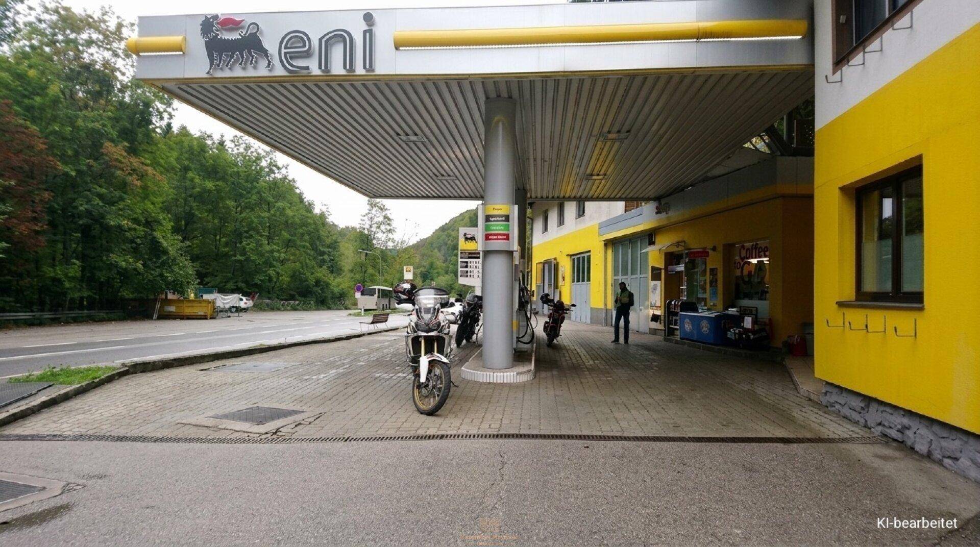 Nahaufnahme des Tankstellendachs mit Zapfsäulen und dem Eingangsbereich des Shops.