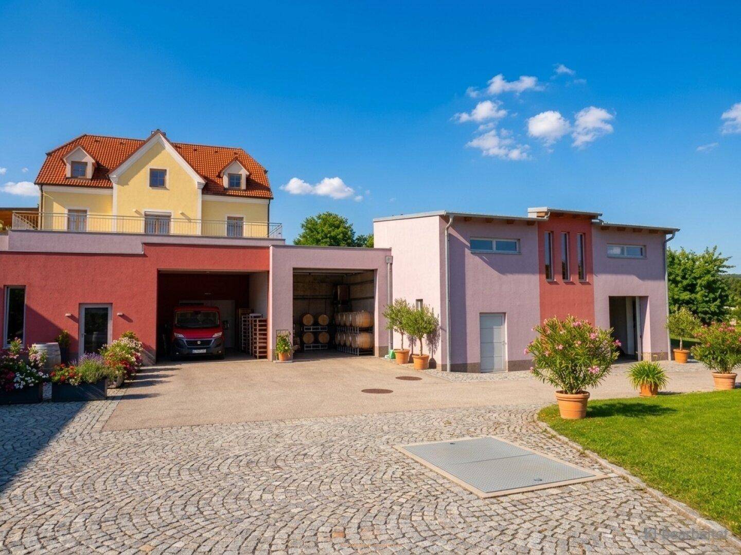 Gebäudeensemble mit großem gepflasterten Hof, Garagen und einem roten Lieferwagen.