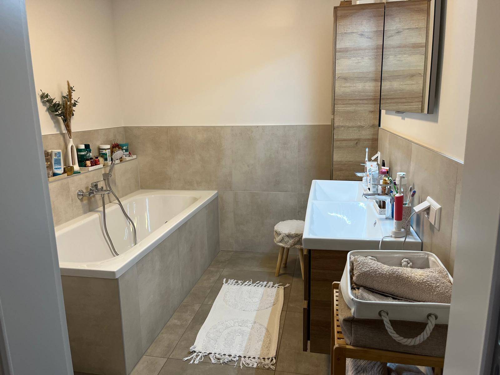 Praktisches Badezimmer mit Badewanne, zwei Waschbecken und hellen Fliesen.