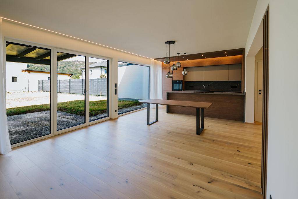 Offener Küchenbereich mit Holzboden, modernen Einbauschränken und großen Schiebetüren zum Garten.