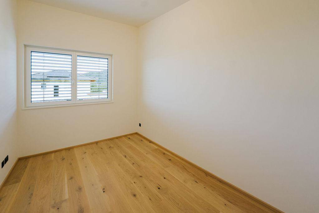 Helles, unmöbliertes Zimmer mit Eichenparkett und einem Fenster mit Außenjalousien.