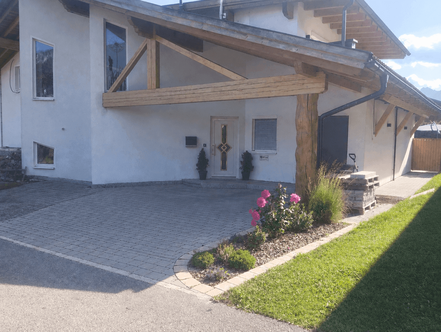 Modernes Einfamilienhaus mit weißer Fassade, Holz-Carport und gepflasterter Einfahrt.
