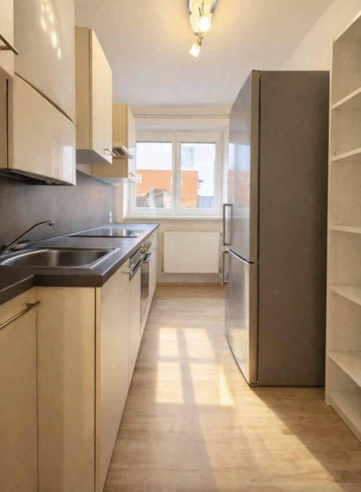 Moderne Küche mit hellen Schränken, Edelstahlspüle und einem großen Kühlschrank.