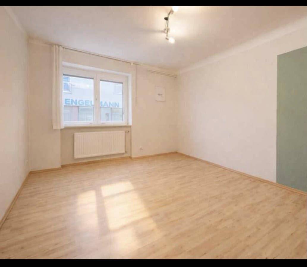 Geräumiges Zimmer mit Laminatboden, großen Fenstern und einem Heizkörper unter dem Fenster.