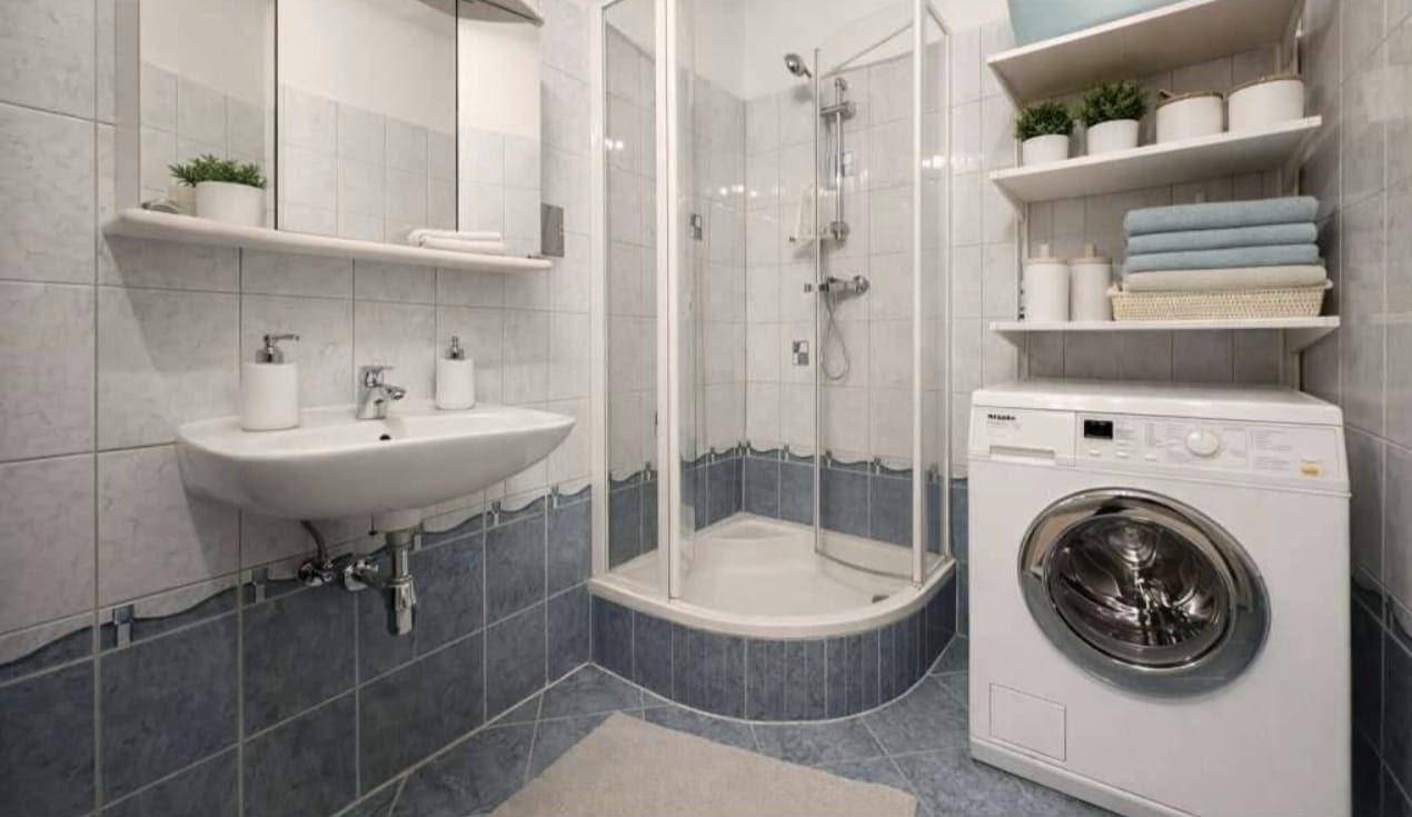 Badezimmer mit Dusche, Waschbecken, Waschmaschine und blauen Fliesen an Wänden und Boden.