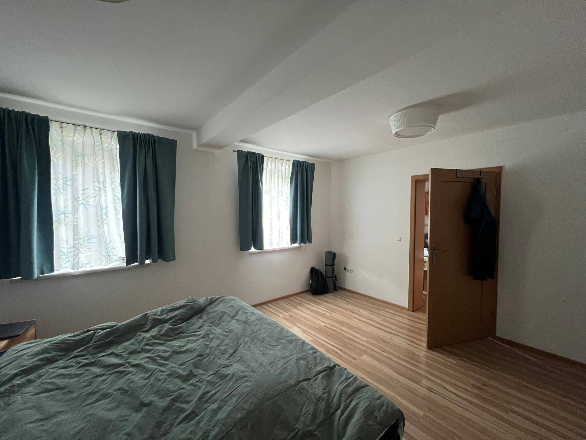 Geräumiges Schlafzimmer mit Laminatboden, zwei Fenstern und einem großen Bett.
