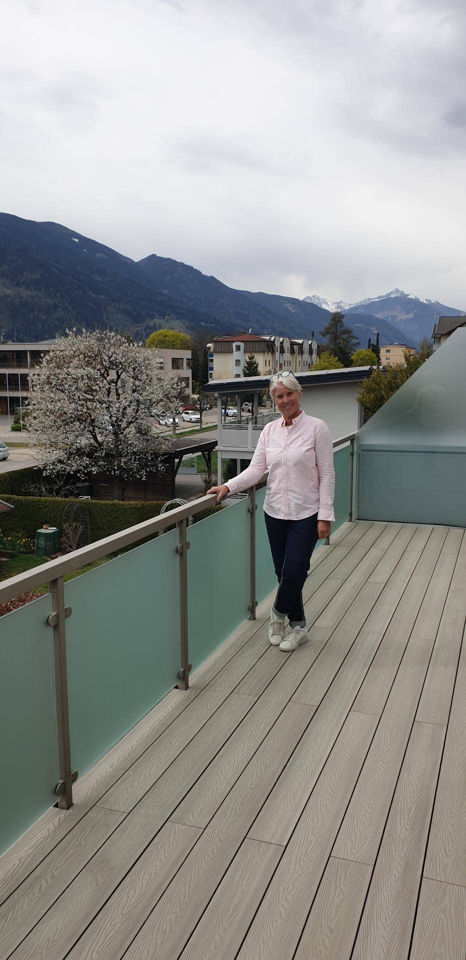 Frau steht auf der Terrasse mit Holzverbunddielen und genießt den weiten Blick auf die Berge und die Umgebung.