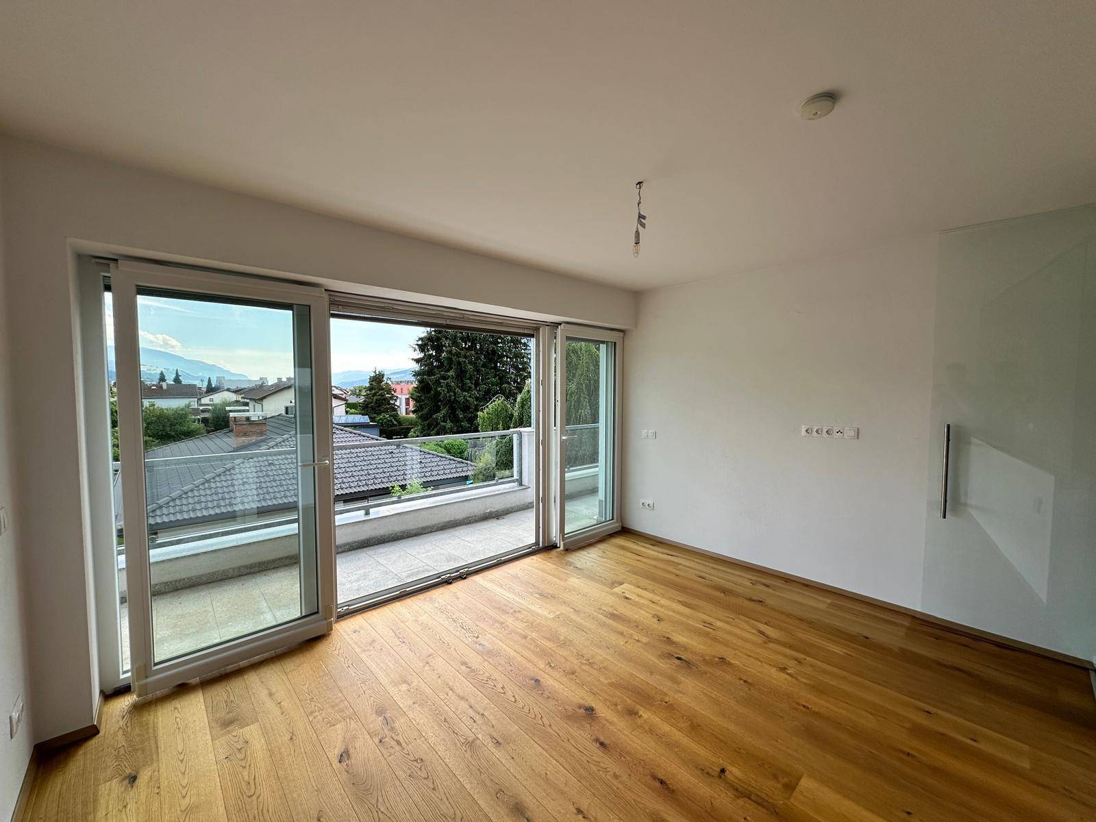 Geräumiges Schlafzimmer mit Holzboden und großen Schiebetüren, die auf eine Terrasse führen.